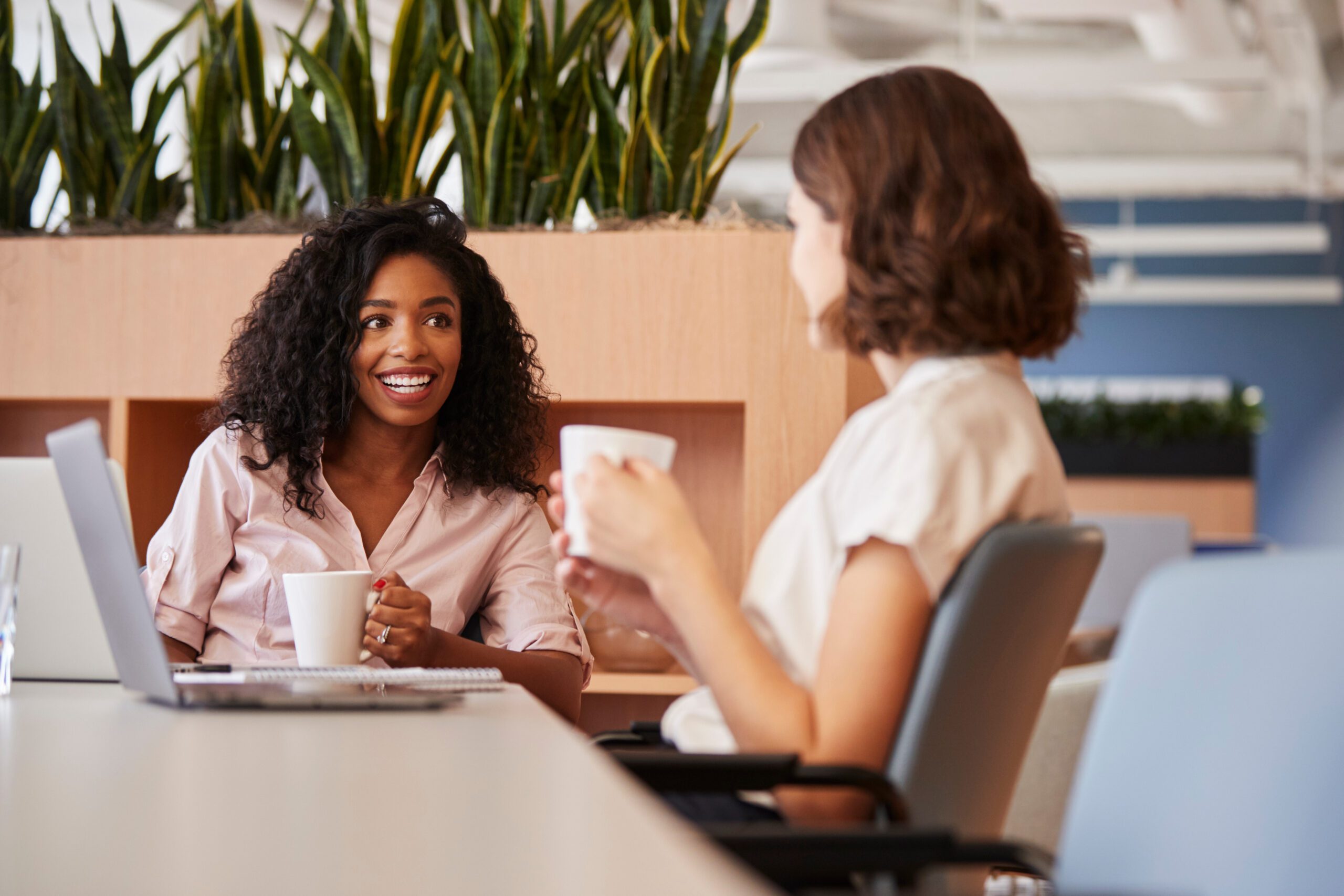 Two businesswomen take a coffee break in an office where HQ video meetings are powered by Kinetic Gig Speed Fiber internet