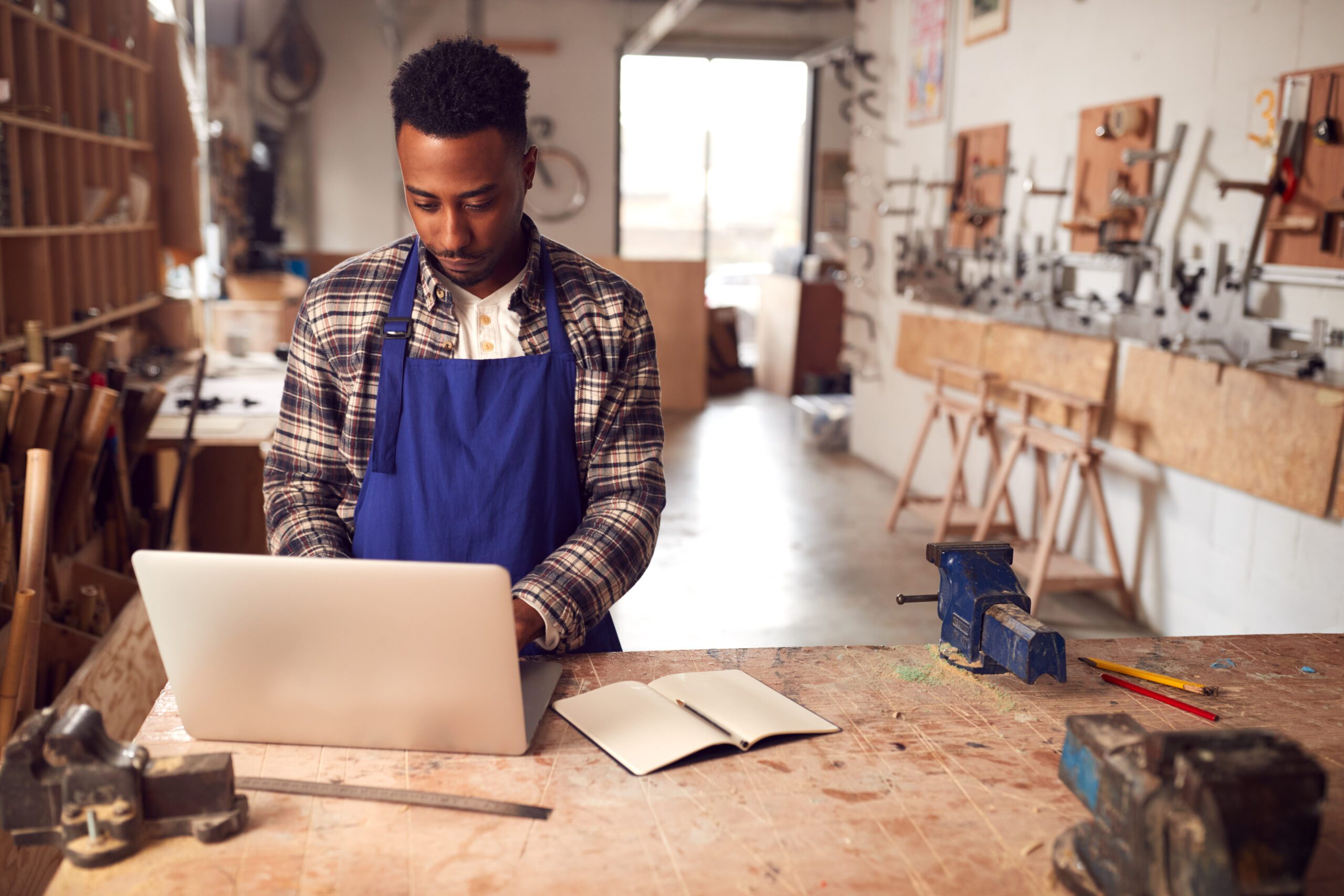 A craftsman at his work bench in a carpentry workshop uses a laptop with business class internet provided by Kinetic Business