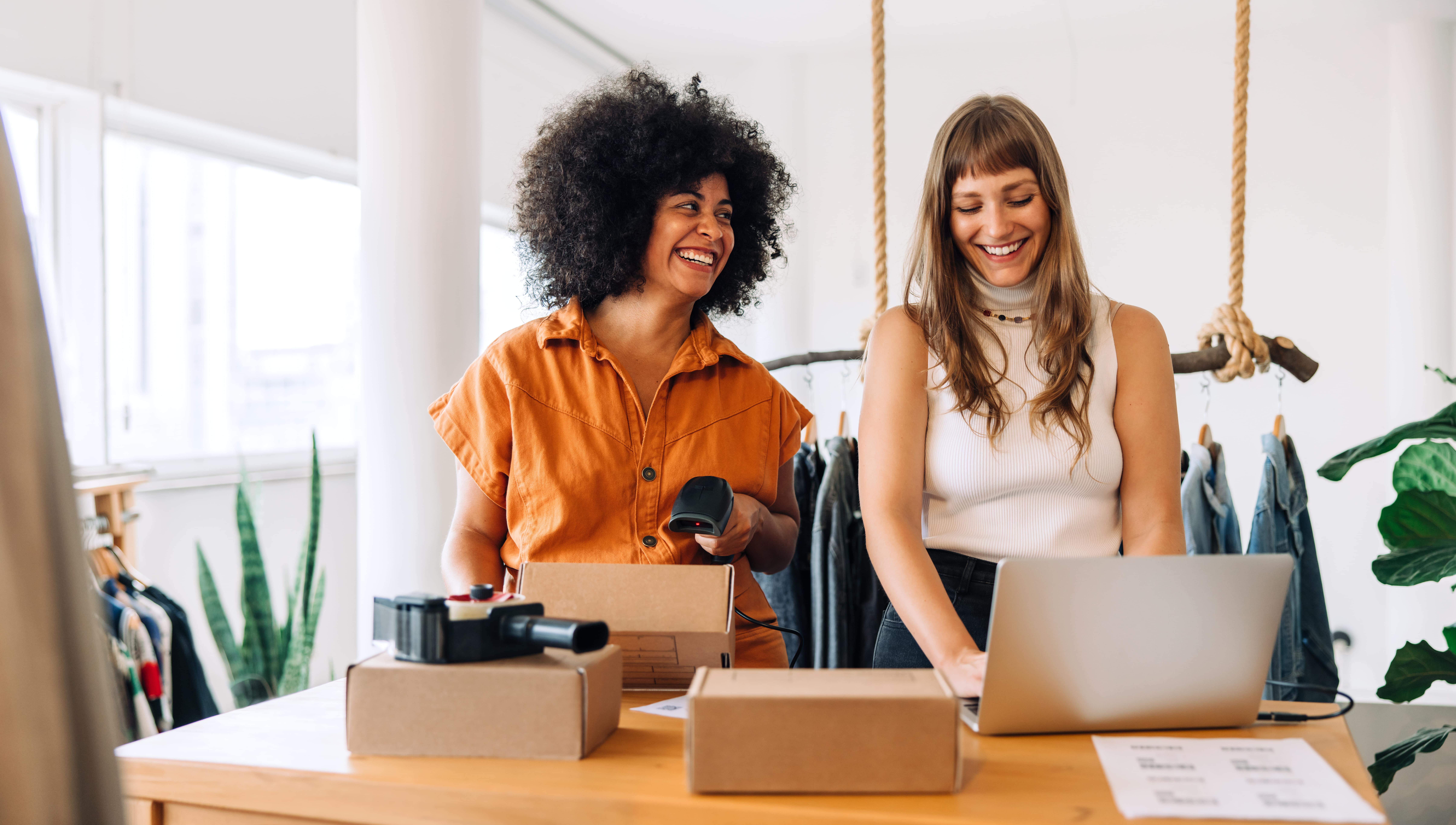 Two female clothing store owners prepare online orders for shipping using a laptop with Kinetic Business internet service.