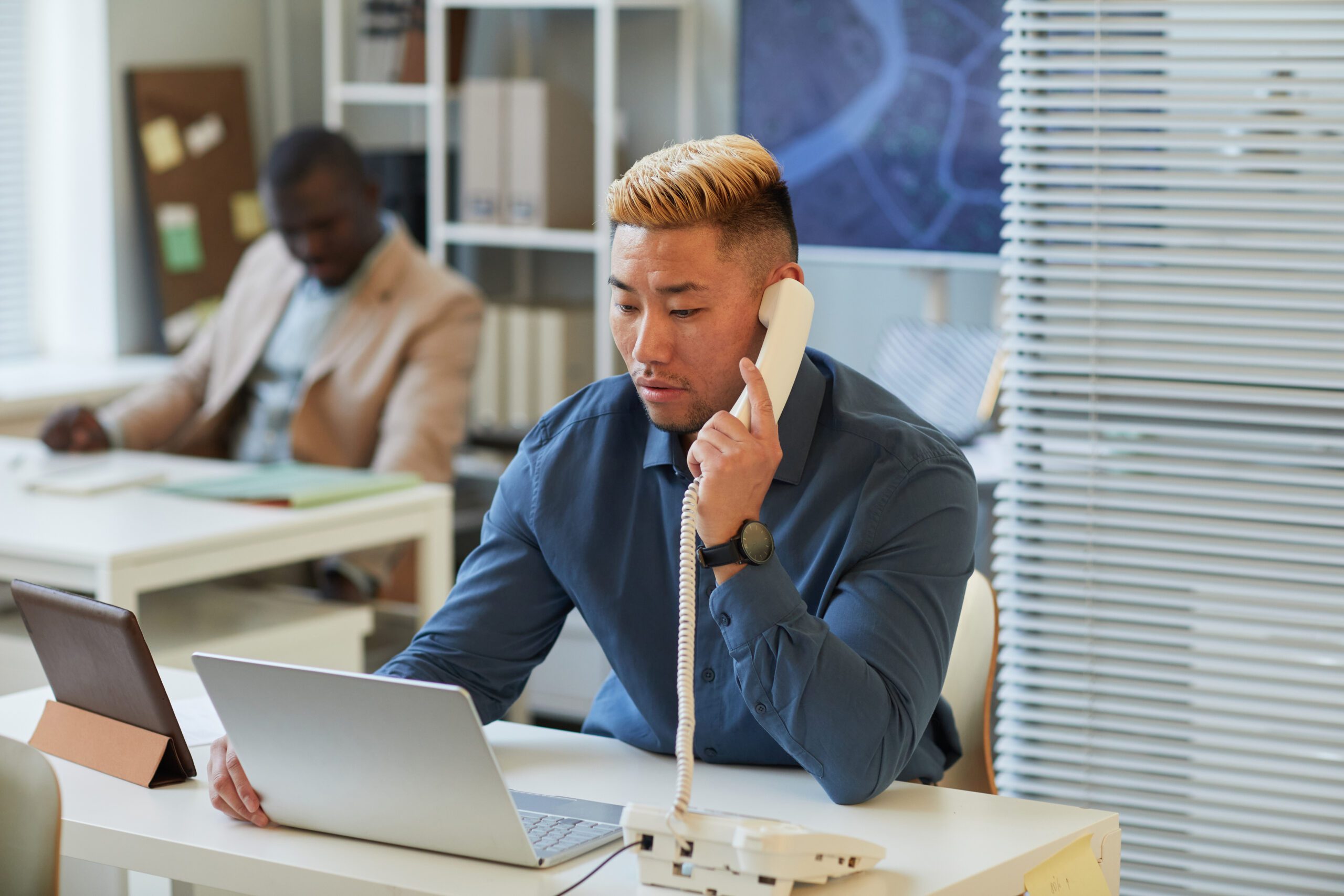 Casual businessman uses a desktop phone and laptop in an office with phone and internet bundled by Kinetic Business 