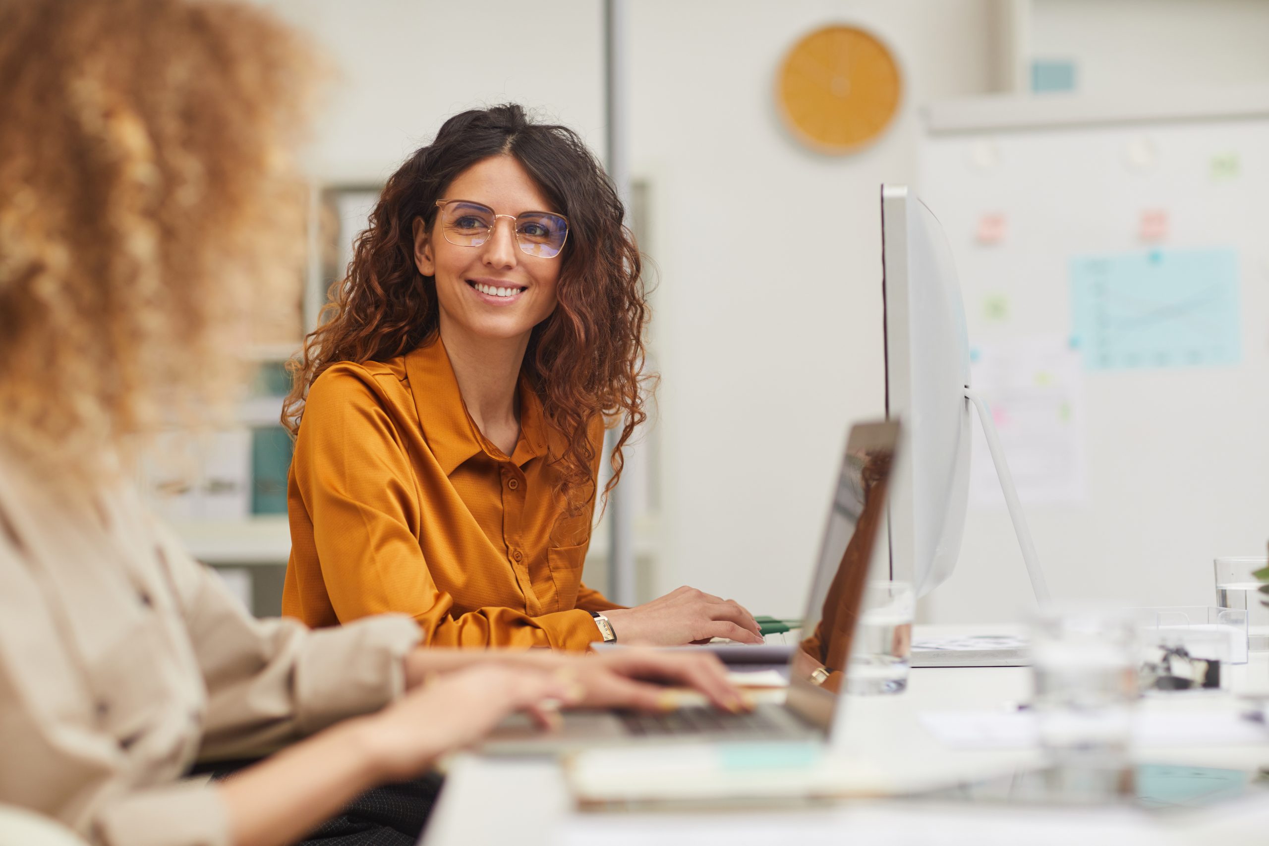 Two female colleagues interacting while working in office on computers