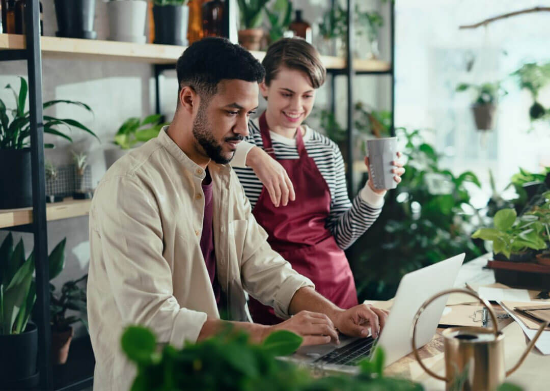 Shop assistants smiling, working on a laptop in a potted plant store that subscribes to Kinetic Business for internet service