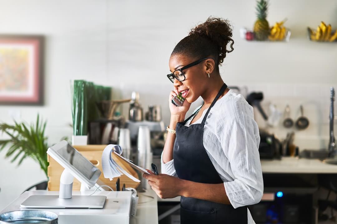 Female retail shop worker in apron using business phone and internet powered by Kinetic Business.