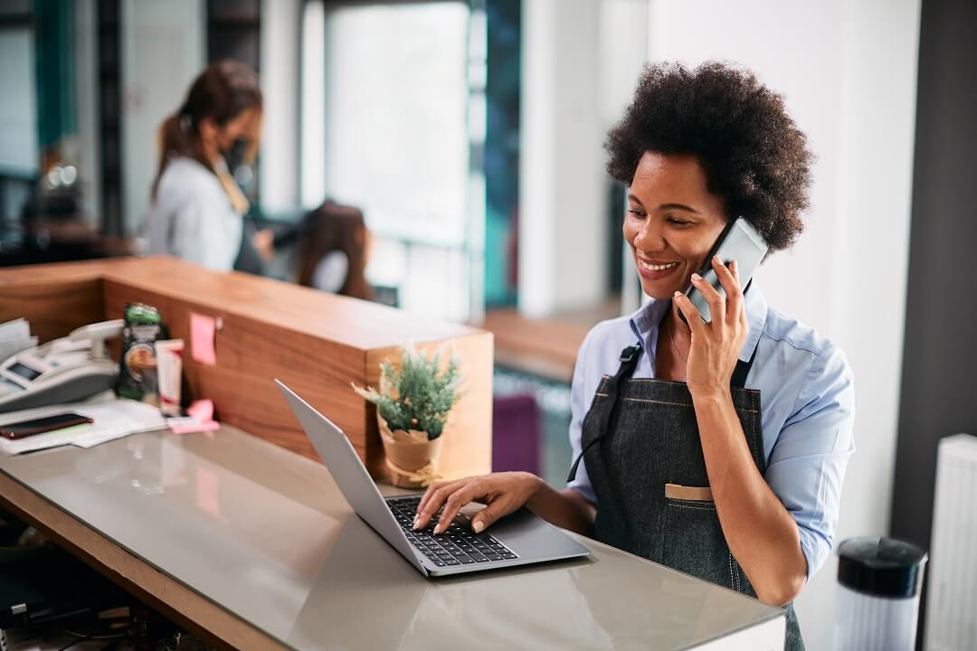 Female retail shop worker wearing apron using business phone and internet powered by Kinetic Business.