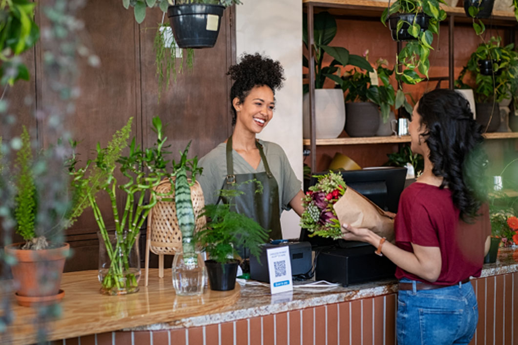 Female retail flower shop owner assisting customer at point of sale checkout.