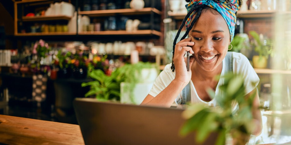 Black female shop owner talking on phone and using laptop.